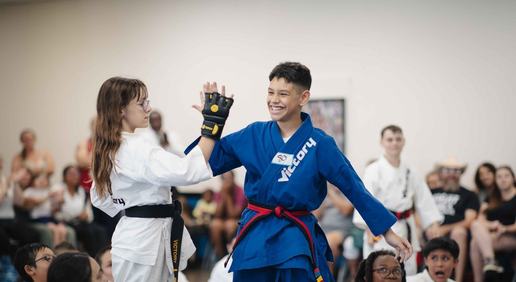 A boy in a blue Victory uniform grins as he high-fives a girl in white, parents watching in the background