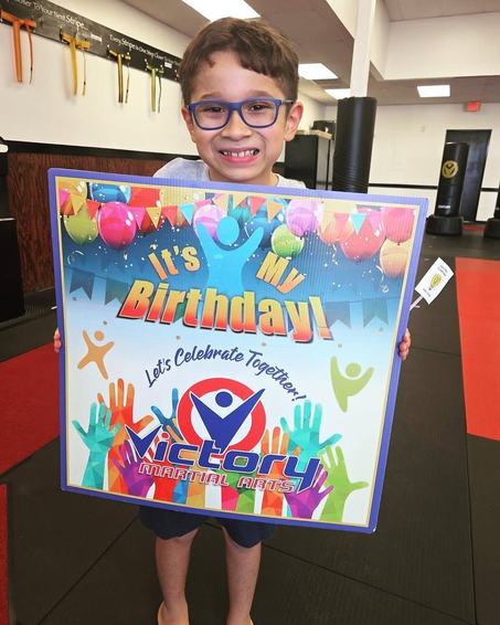 A grinning boy holds his It's My Birthday sign at the studio