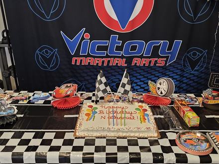 A race-car birthday cake waits on the party table at a Victory studio