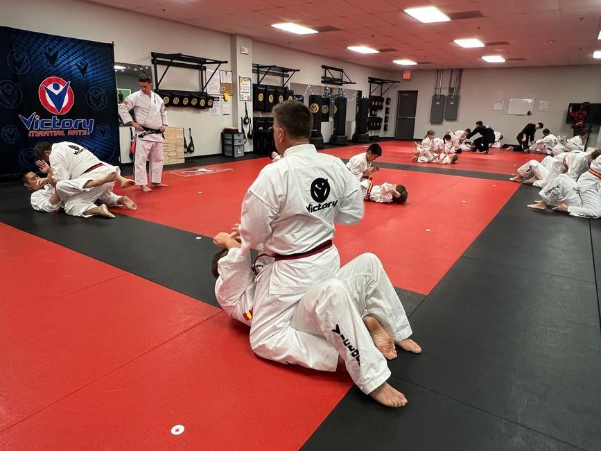 Two students in gis grapple on the mat, one passing the other's guard